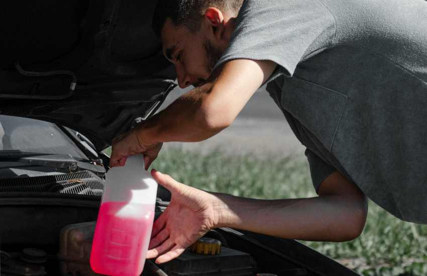 An image of a man putting antifreeze in his car for this blog post that that talks about why antifreeze is toxic to dogs.