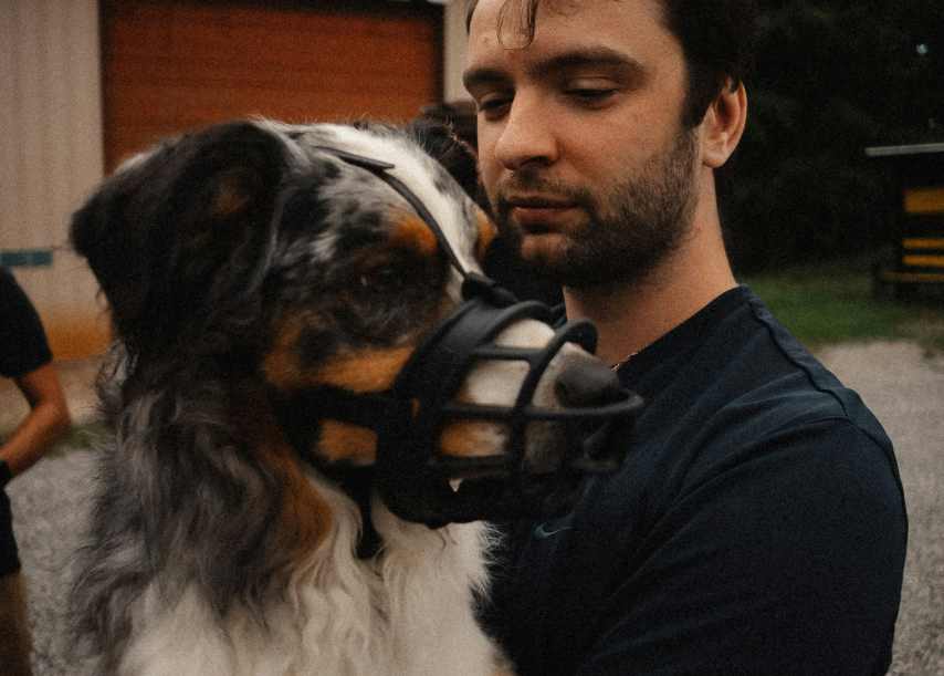 A dog owner holding his dog that is wearing a adjustable dog muzzle. Train your dog with a muzzle.