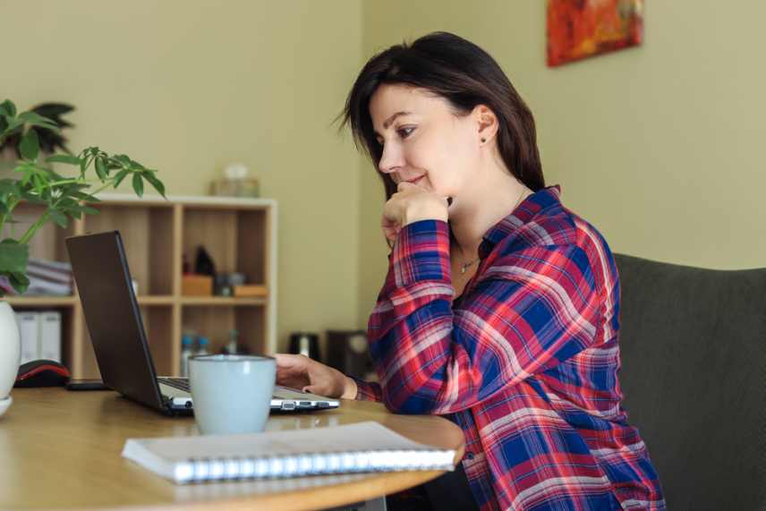 A woman in plaid shirt using laptop to access a free online dog obedience training course.