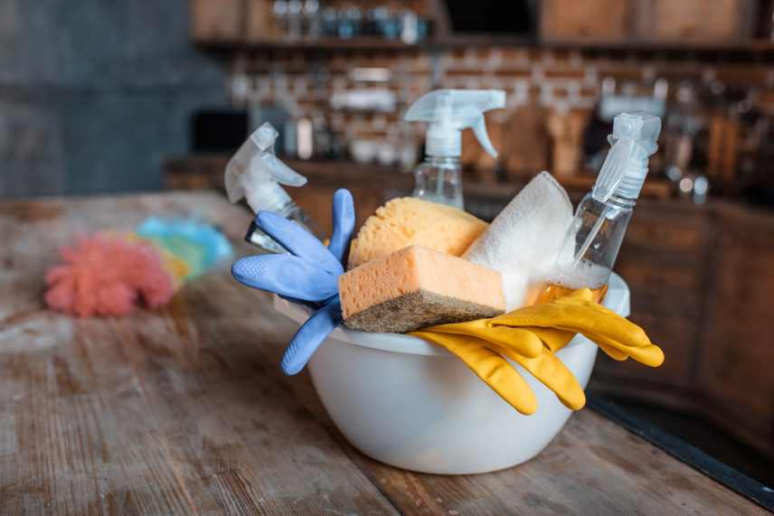 A plastic bowl full of cleaning products sitting on a wooden bench top.